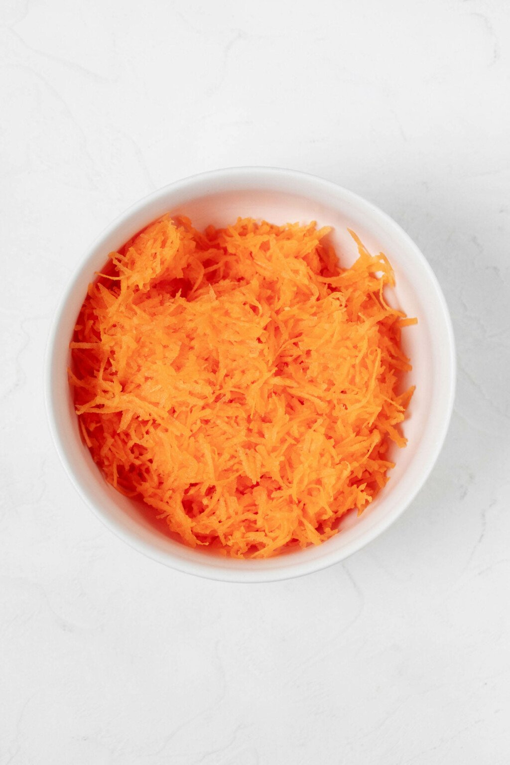 An overhead image of finely grated carrots, nestled in a round white bowl.