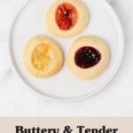 A round, rimmed dessert plate rests on a marble surface. It holds three jam filled sugar cookies.