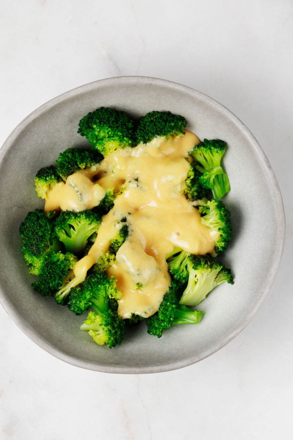 Een kom gestoomde broccoli is omhuld met een vegan cheddar kaassaus.