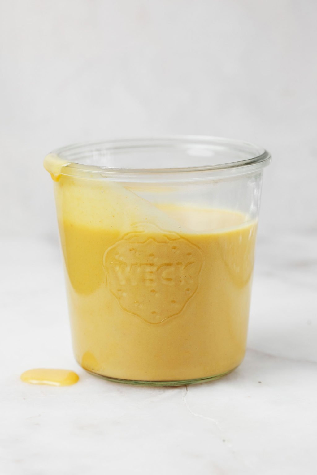 Een glazen pot bevat gele vegan cheddar kaassaus.