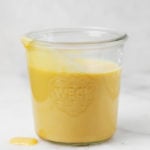 Un frasco de vidrio contiene una salsa de queso cheddar vegana amarilla.