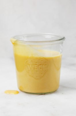 A glass mason jar holds a yellow, vegan cheddar cheese sauce.