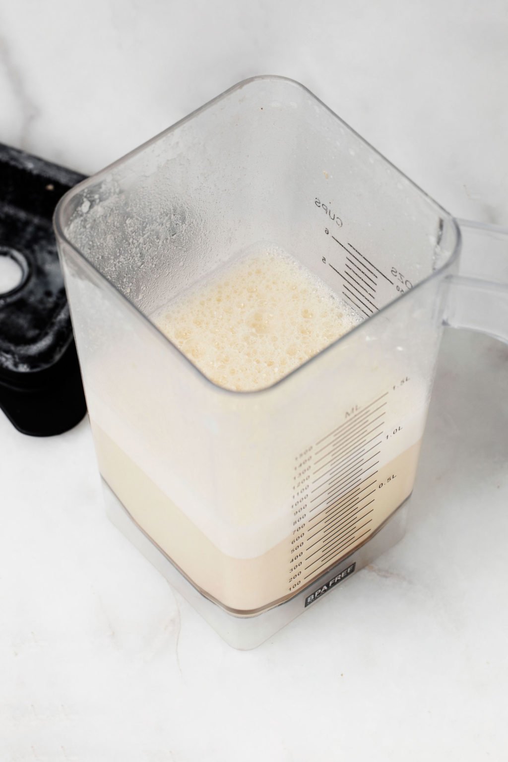 A blender contains non dairy milk. It rests on a white marble surface.