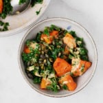 Two bowls of warm winter squash and steamed kale rest on a white marble surface.