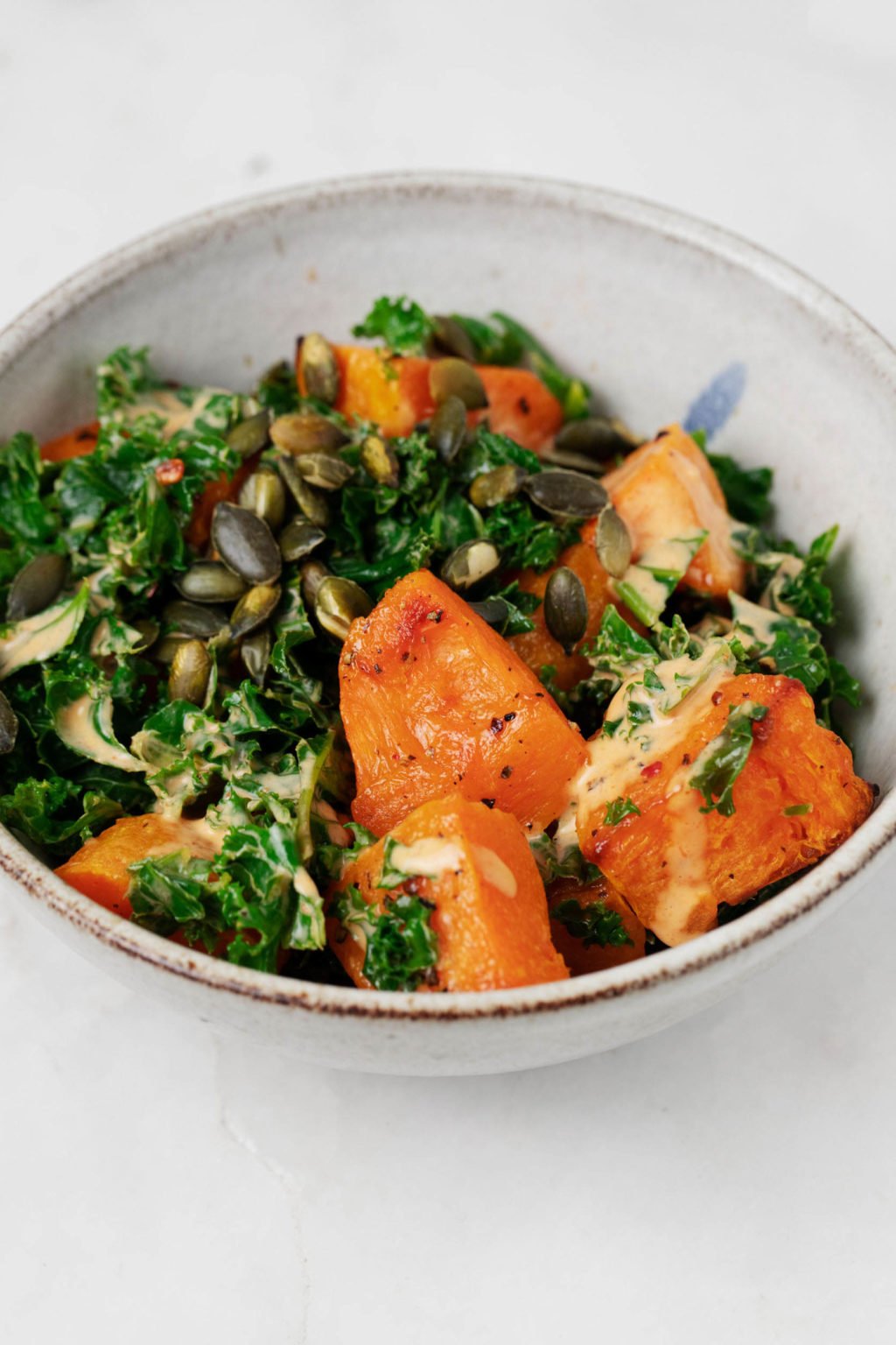 A serving of warm winter vegetables and steamed kale has been topped with toasted pepitas and a creamy dressing.