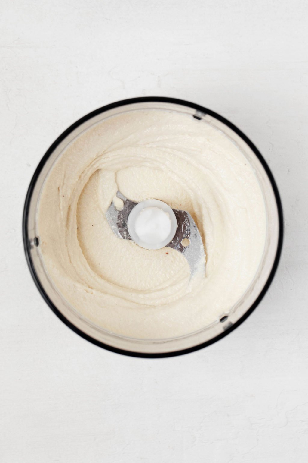 An overhead image of a food processor, which is filled with a creamy white mixture.