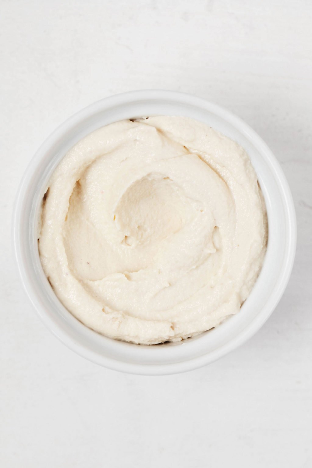 An overhead image of a small, white pinch bowl filled with vegan ricotta cheese.