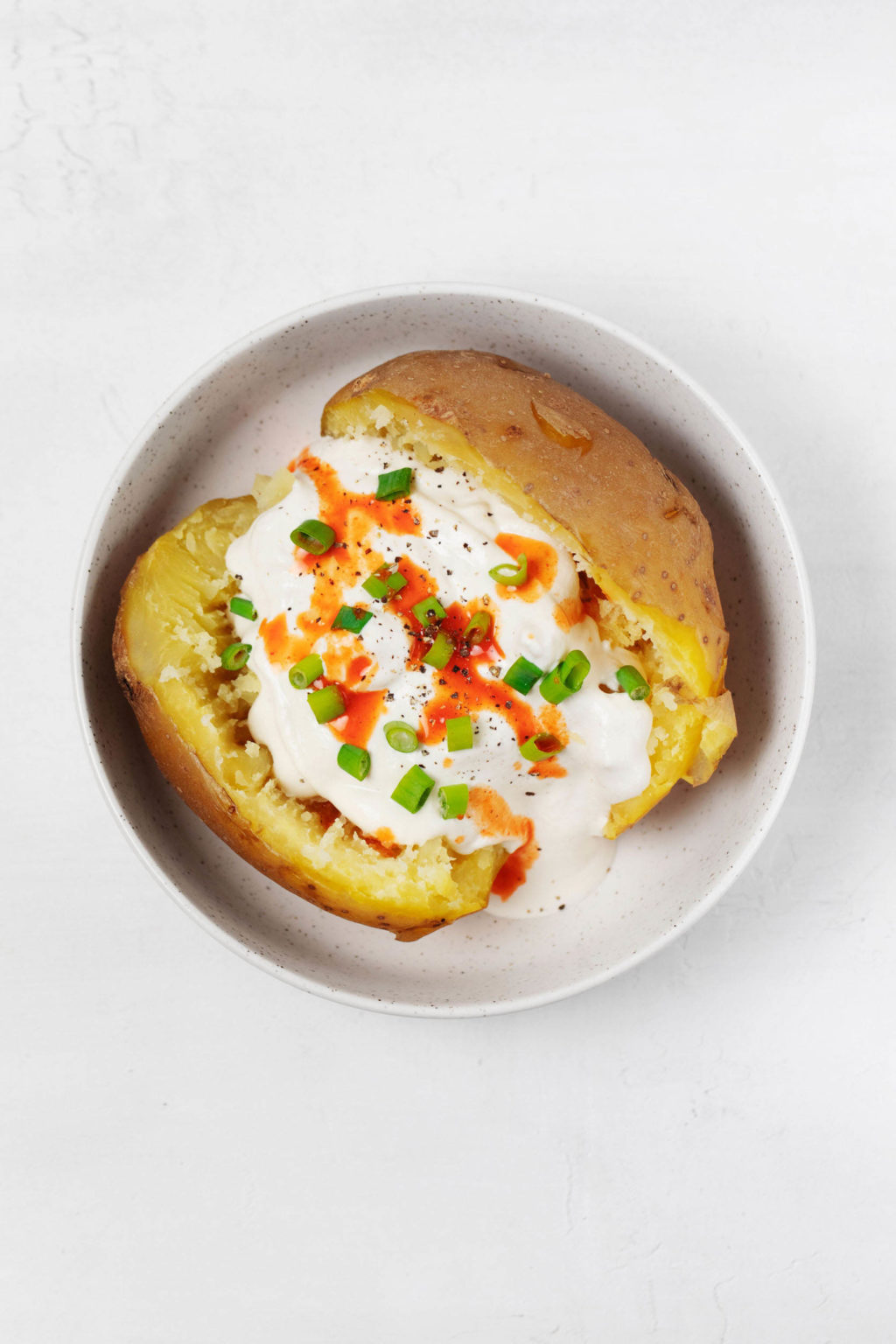 An overhead image of a baked sweet potato, topped with vegan sour cream, chives, and hot sauce.