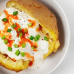 An overhead image of a split, baked potato, which is topped with chives, hot sauce, and other toppings.