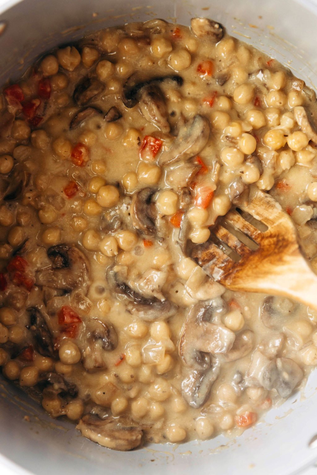 A dish of mushrooms and beans is simmering in a skillet. Dots of red pepper are distributed through the dish.