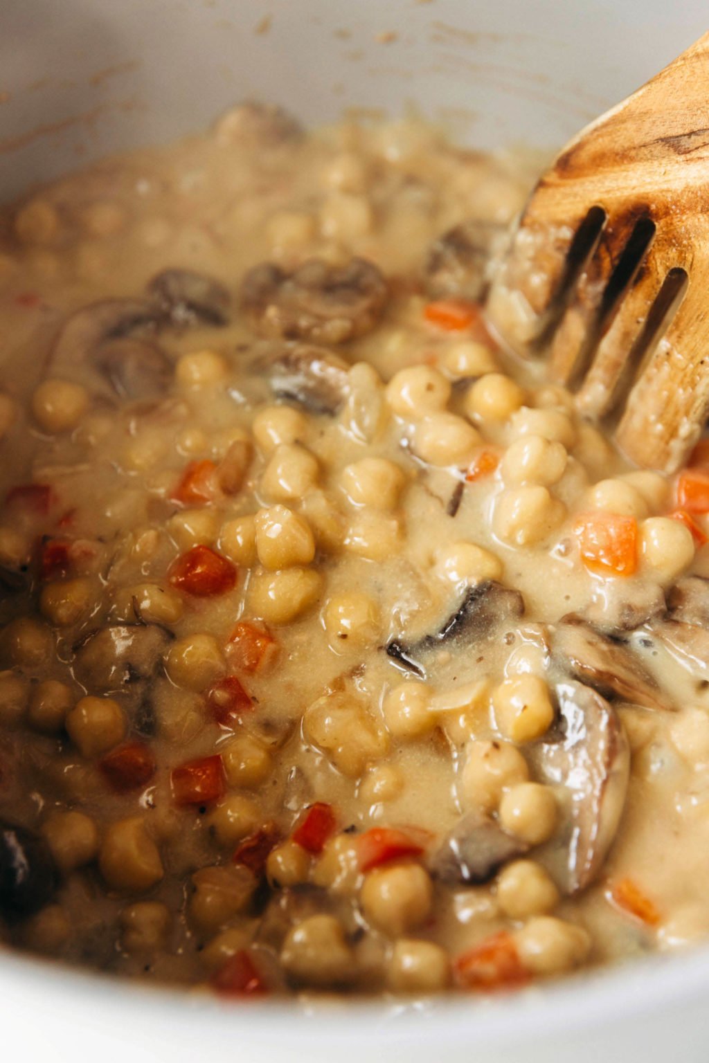 Chickpeas, mushrooms, and red peppers are simmering in liquid in a skillet.