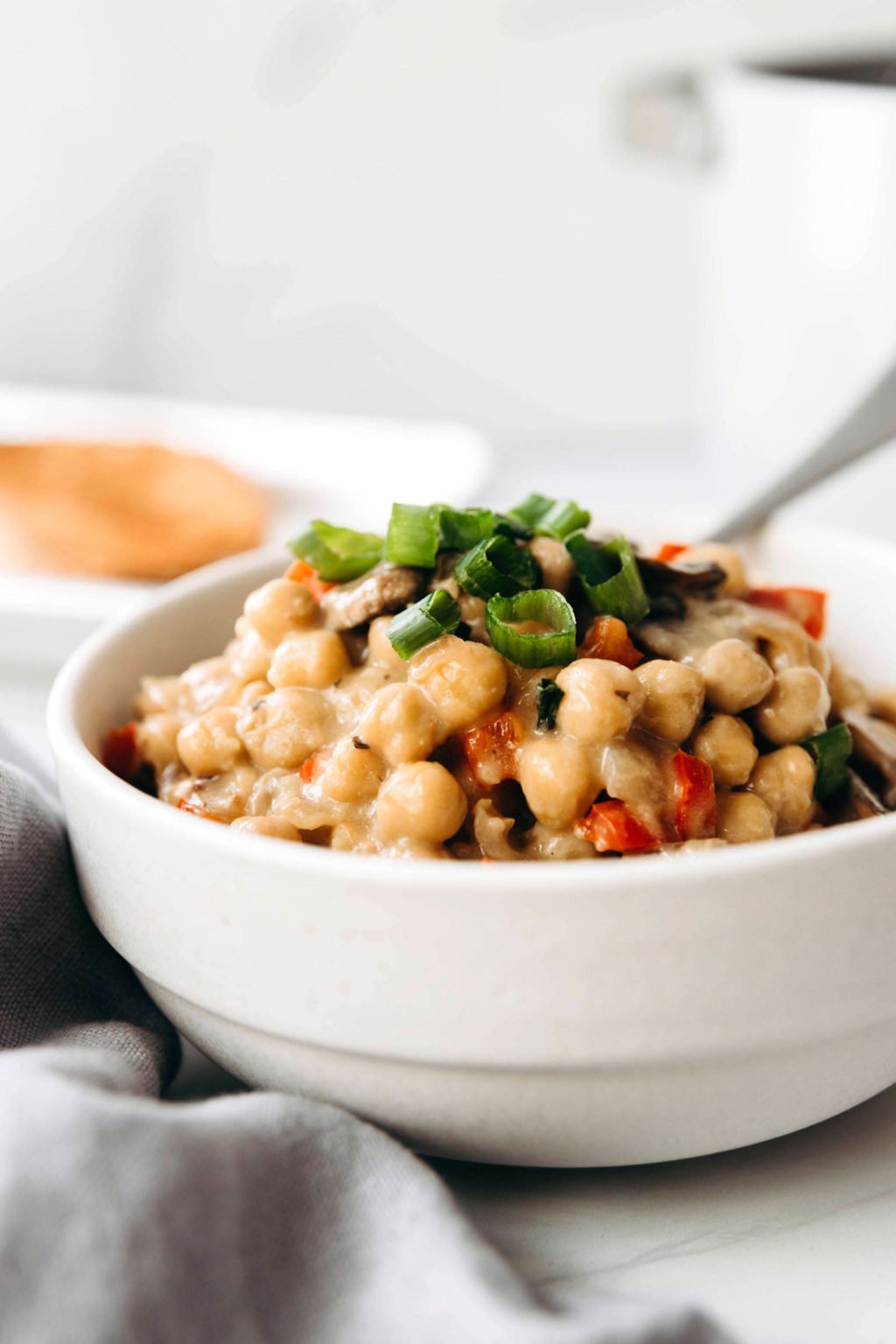 A white bowl holds a vegan dish of chickpeas à la King, topped with chopped, green scallion tops.