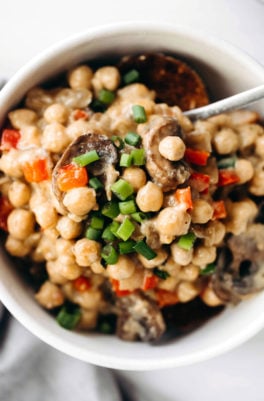 A close, overhead image of cooked beans, chopped scallions, and red peppers with mushrooms.