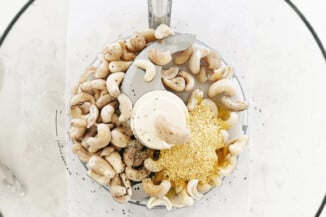 Cashews and nutritional yeast are pictured in the bowl of a food processor.