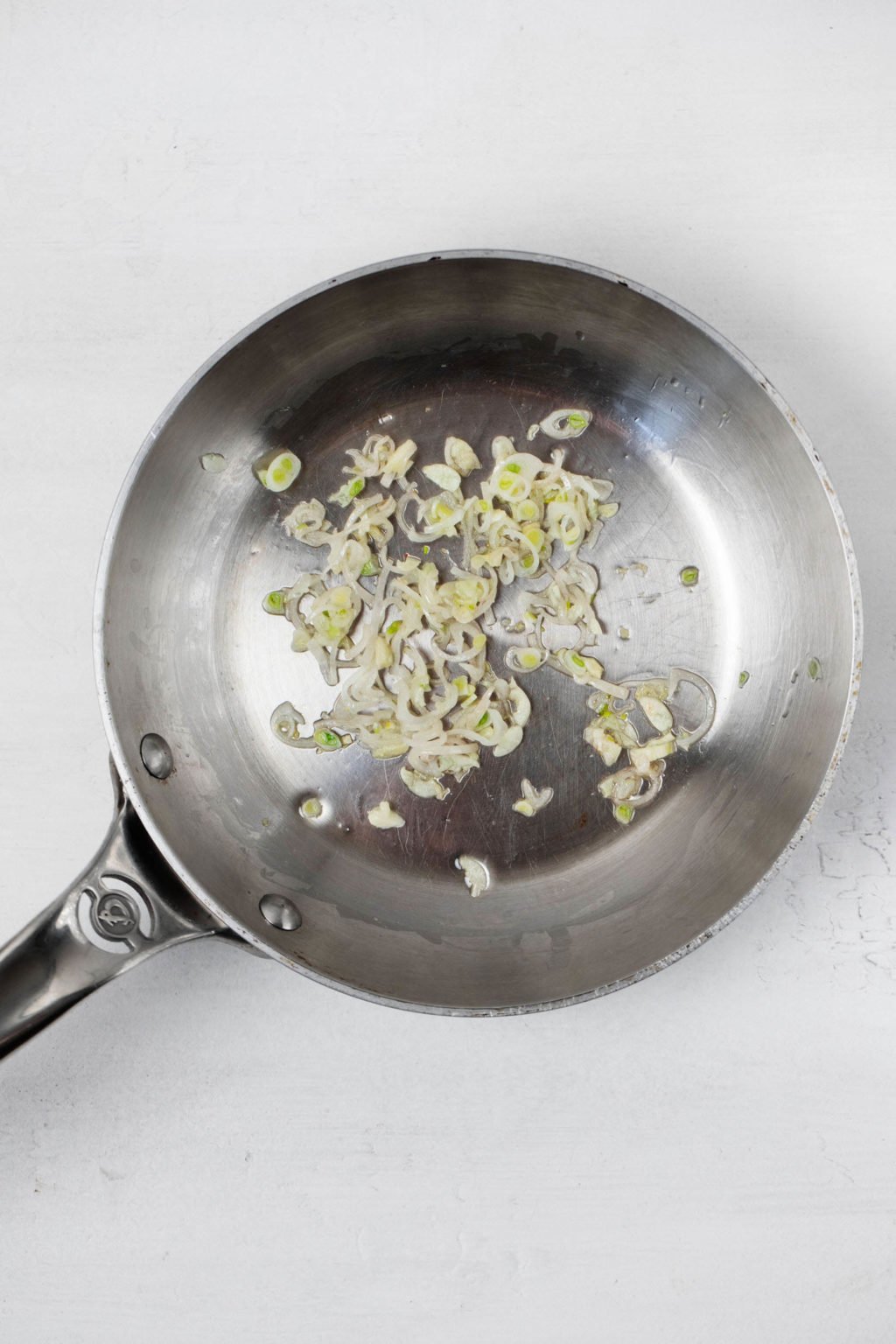 A small, silver frying pan is being used to cook thinly sliced shallots.
