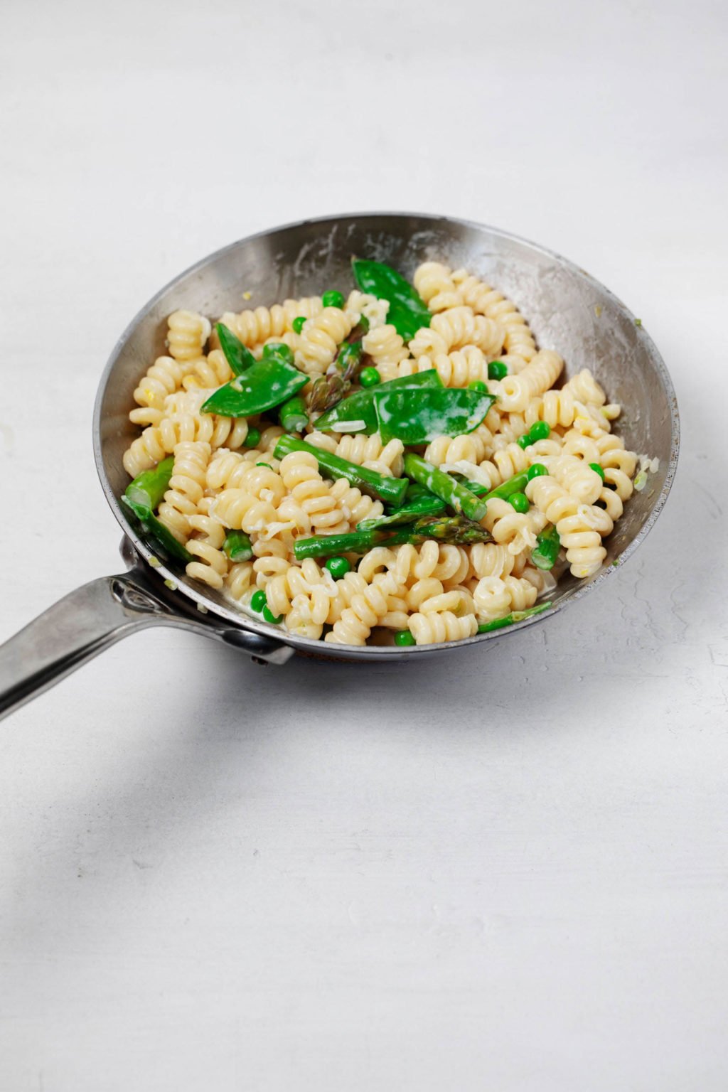 A silver saucepan is filled with pasta and vegetables.