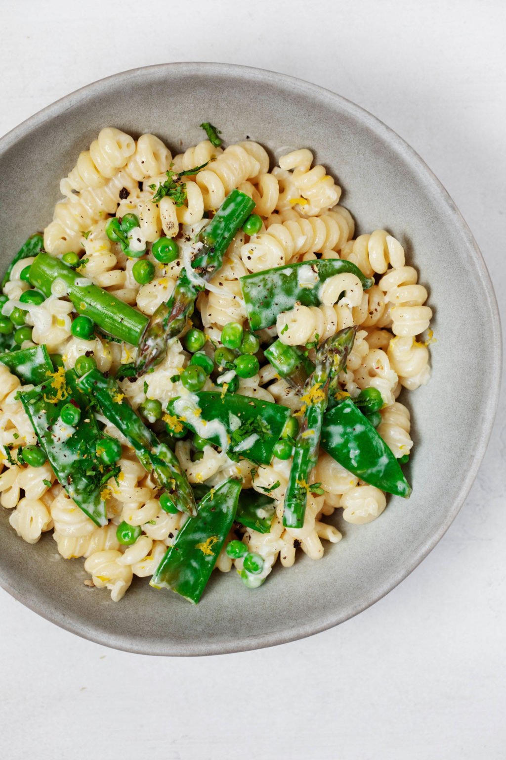 An overhead image of a bowl of vegan spring pasta primavera, which is packed with bright green vegetables.