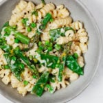 An overhead image of a bowl of vegan spring pasta primavera, which is packed with bright green vegetables.