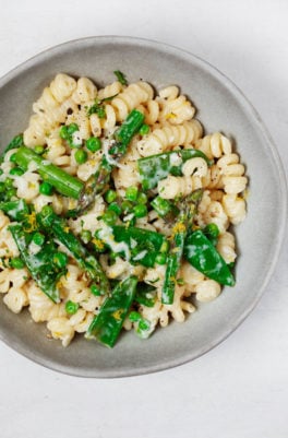An overhead image of a bowl of vegan spring pasta primavera, which is packed with bright green vegetables.
