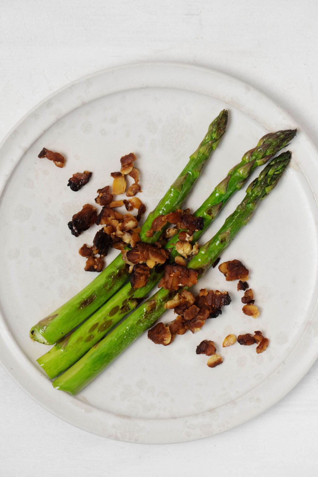 A round, white plate holds freshly cooked asparagus spears. It rests on a white surface.