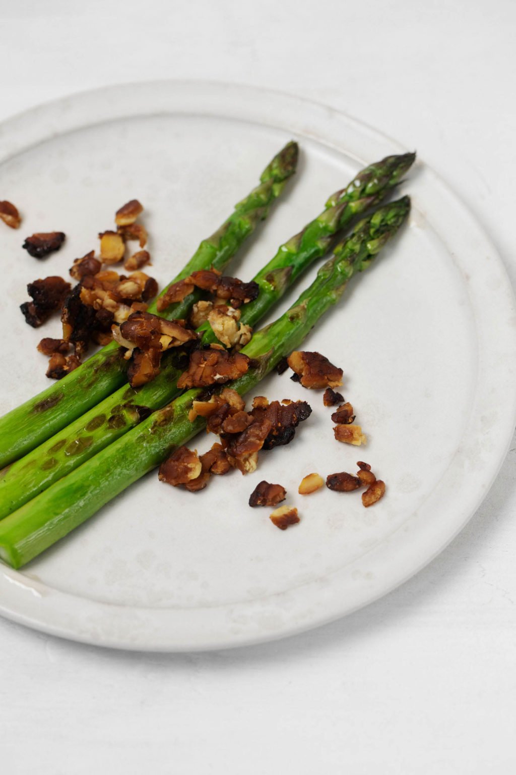Green asparagus spears have been topped with a plant-based, crumbled tempeh "bacon."