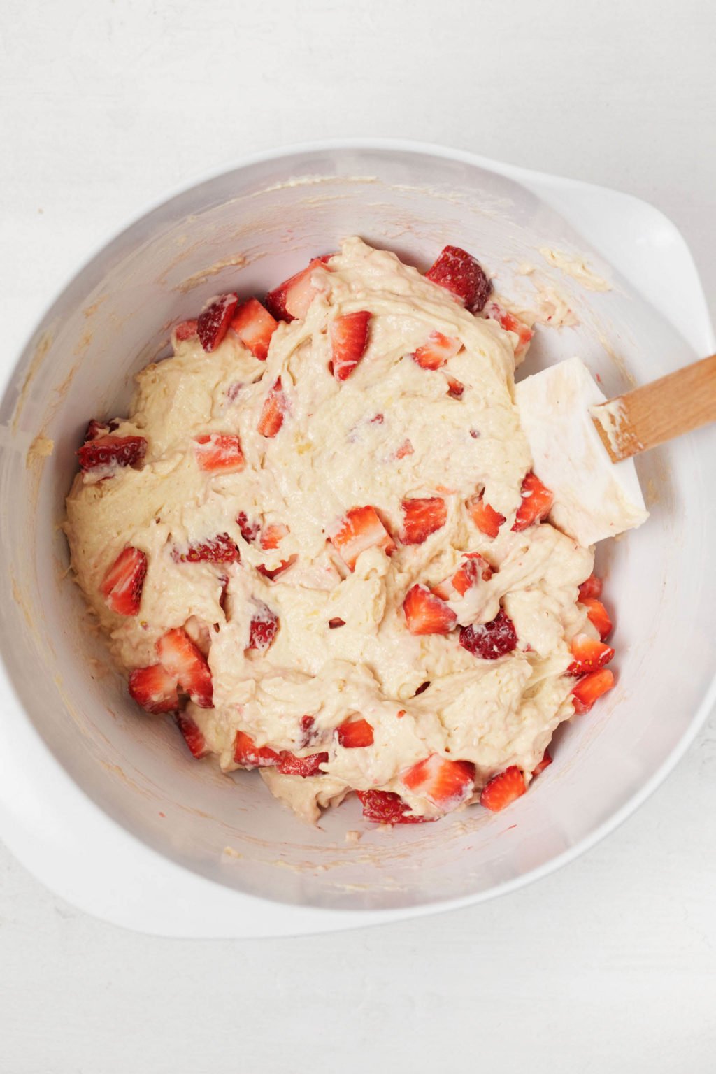 An overhead image of a white bowl of batter for baked goods, which is specked with pieces of fresh fruit.