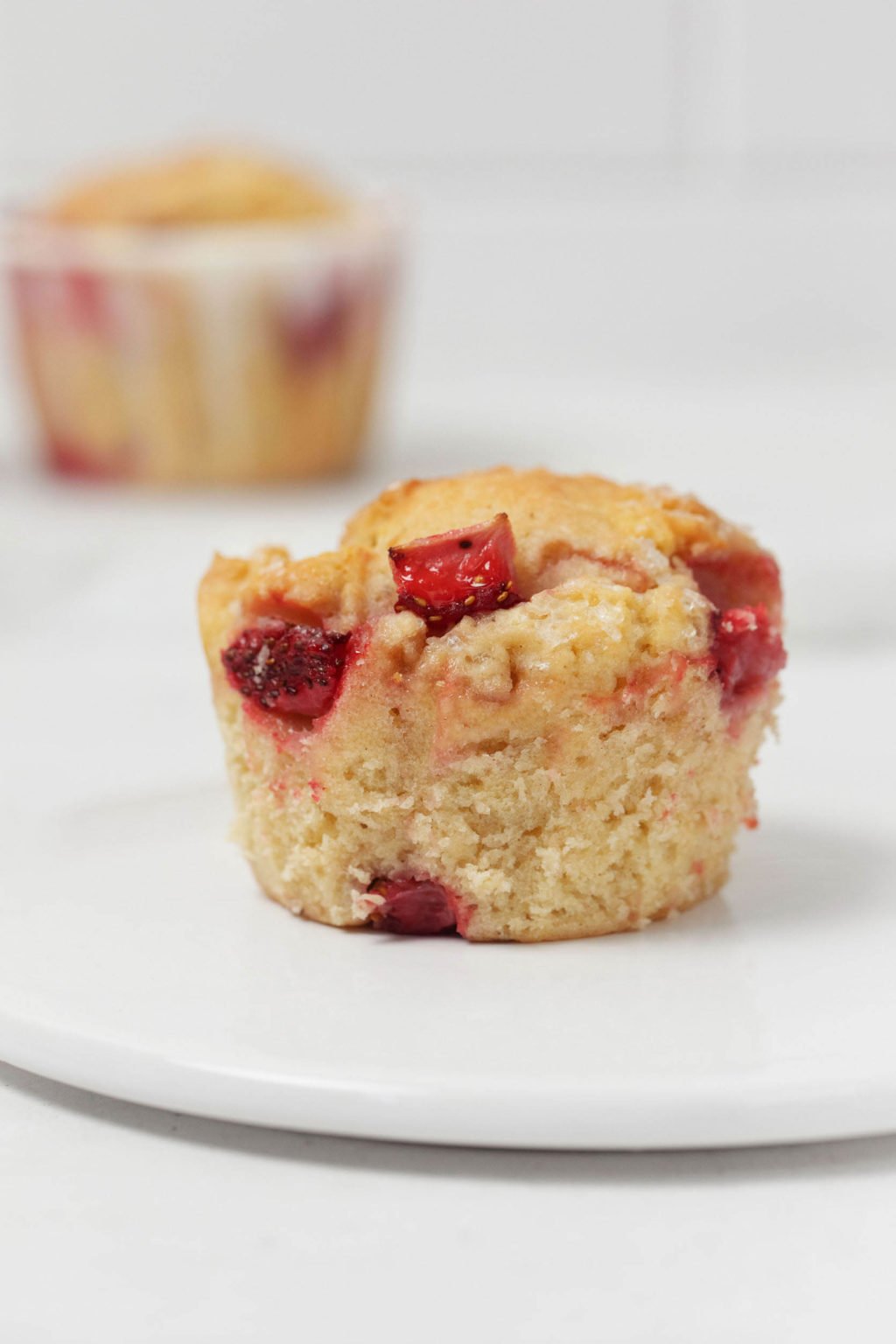 A small, round, white serving plate has been topped with a single vegan strawberry muffin.