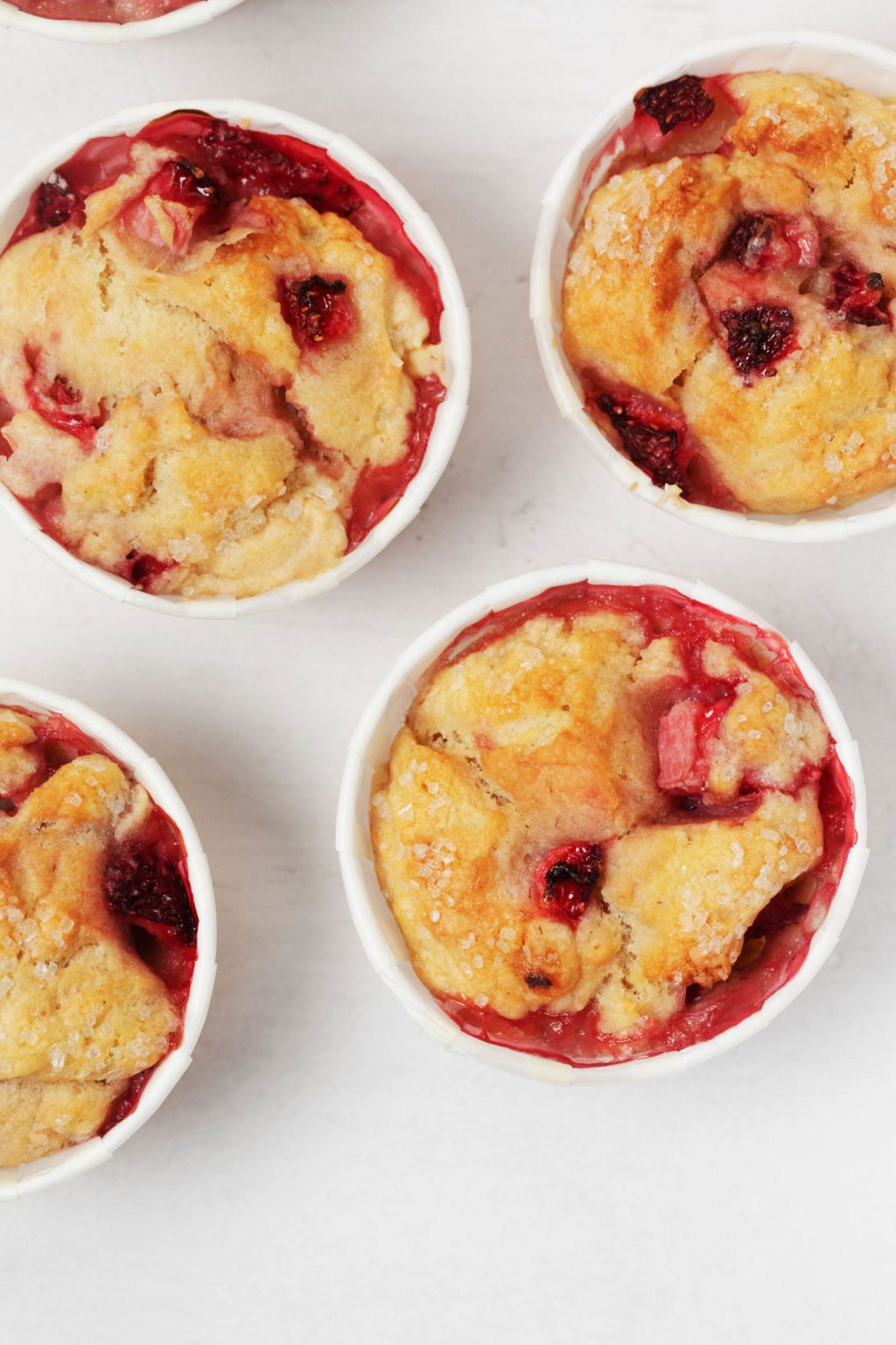 Vegan strawberry muffins, baked in white muffin liners, are resting on a white surface.