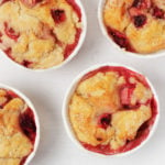 Vegan strawberry muffins, baked in white muffin liners, are resting on a white surface.