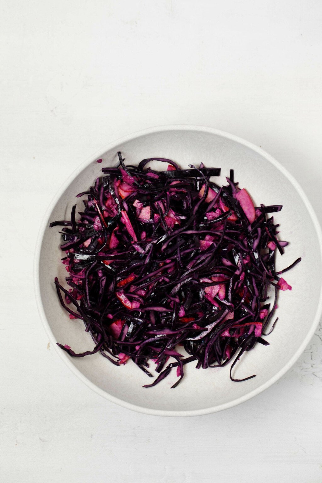 A white bowl is filled with a slaw of red cabbage and apple.