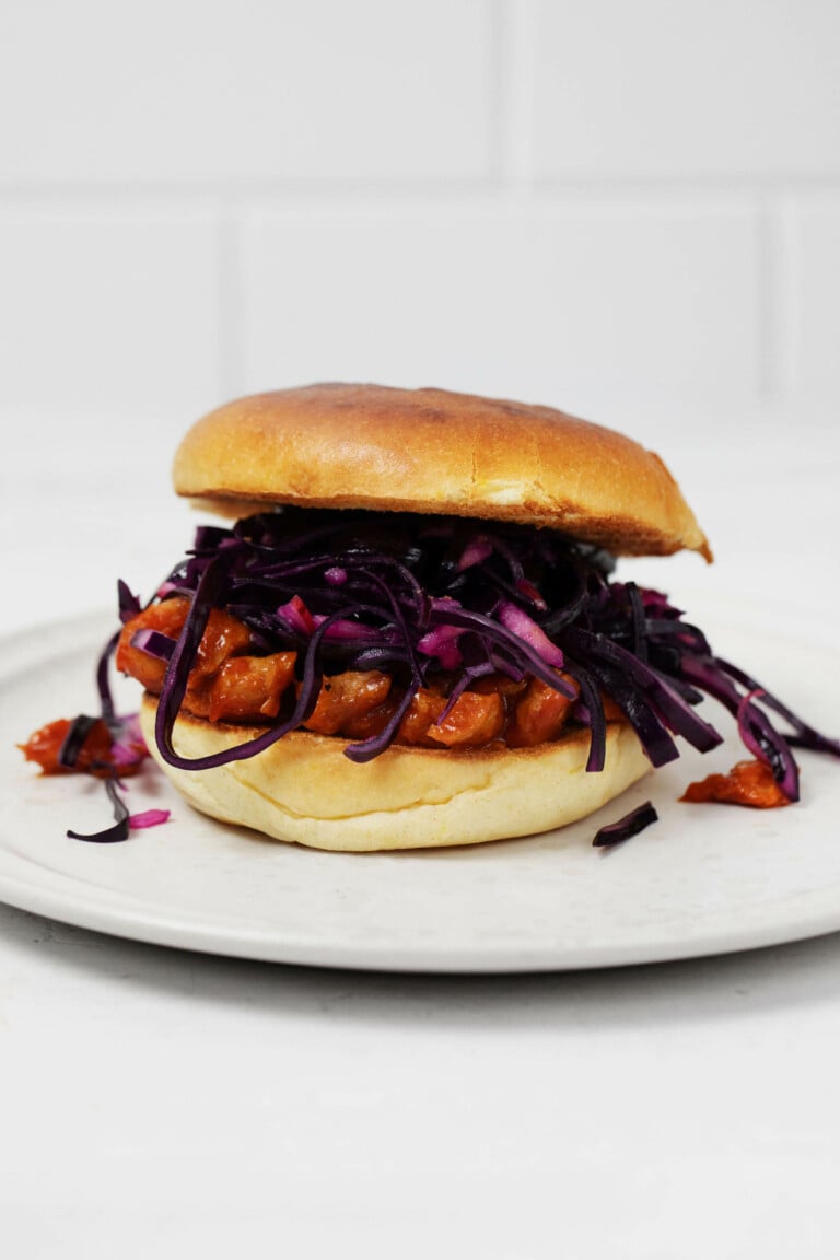 An angled photograph of a burger bun piled with vegan barbecue soy curls and a crispy cabbage slaw.