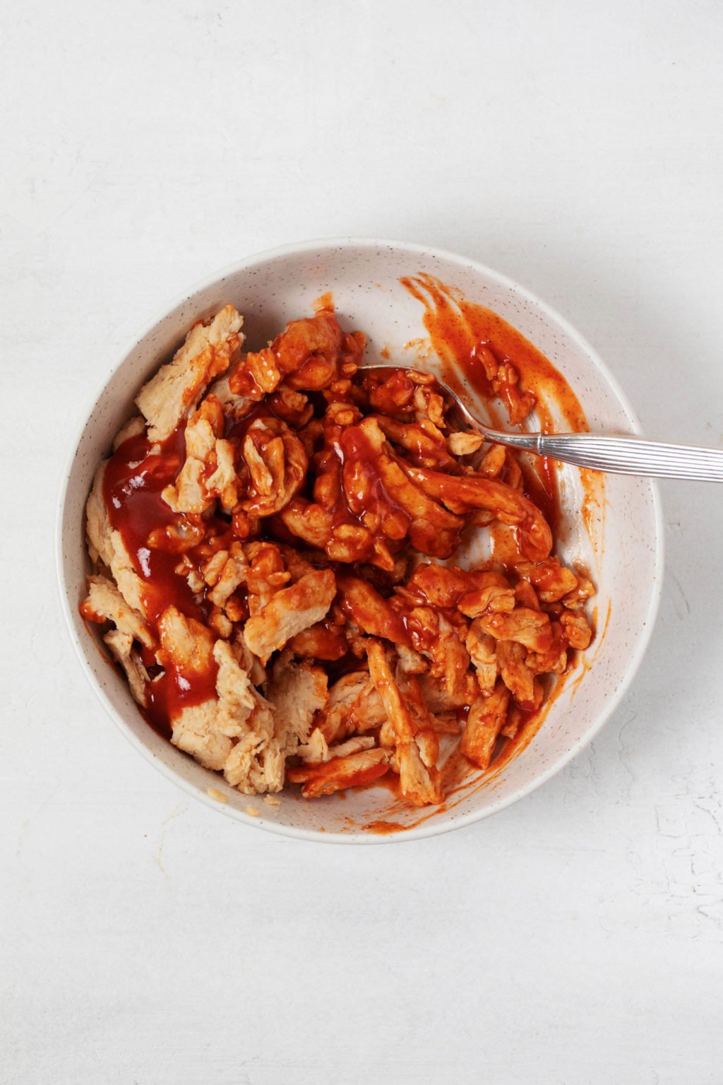 Soy curls are being coated with red sauce in a mixing bowl.