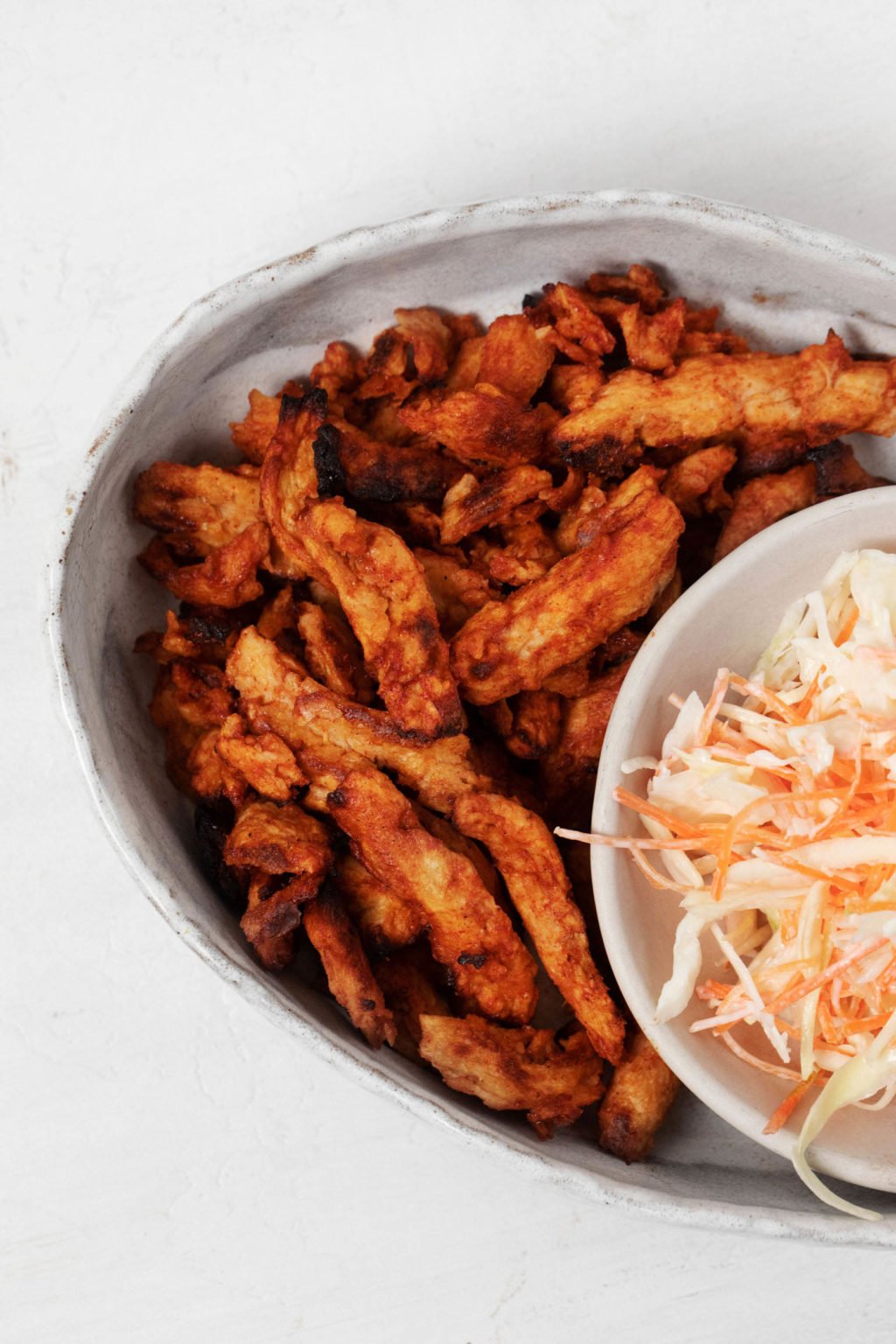 BBQ soy curls are nestled next to a small bowl of coleslaw on an oval serving platter.