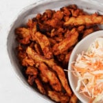 BBQ soy curls are nestled next to a small bowl of coleslaw on an oval serving platter.