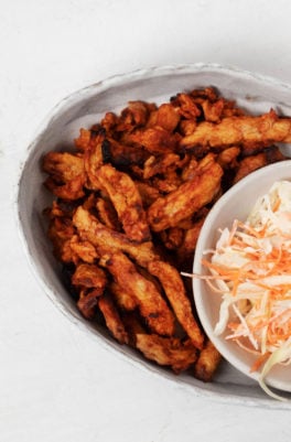 BBQ soy curls are nestled next to a small bowl of coleslaw on an oval serving platter.