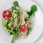 A white, rimmed plate serves a brown rice and spinach salad with asparagus and grape tomatoes.