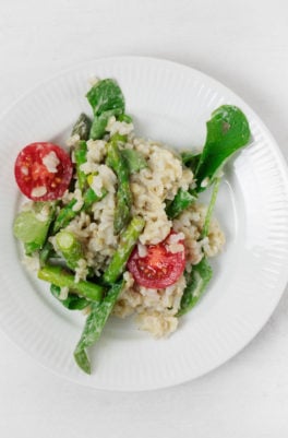 A white, rimmed plate serves a brown rice and spinach salad with asparagus and grape tomatoes.