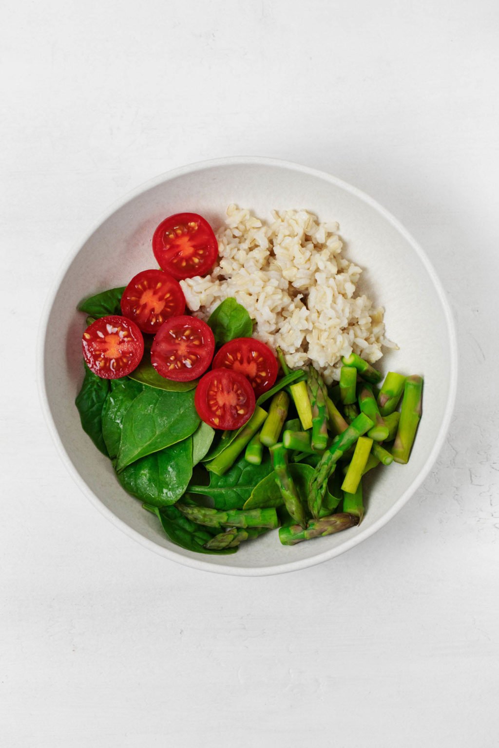 A round, white bowl holds fresh summer vegetables and a cooked whole grain.
