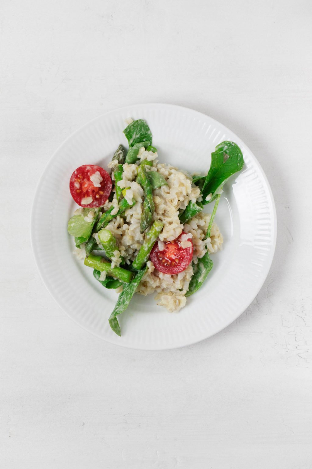 A round, white rimmed plate has been filled with a brown rice and spinach salad. It rests on a white surface.