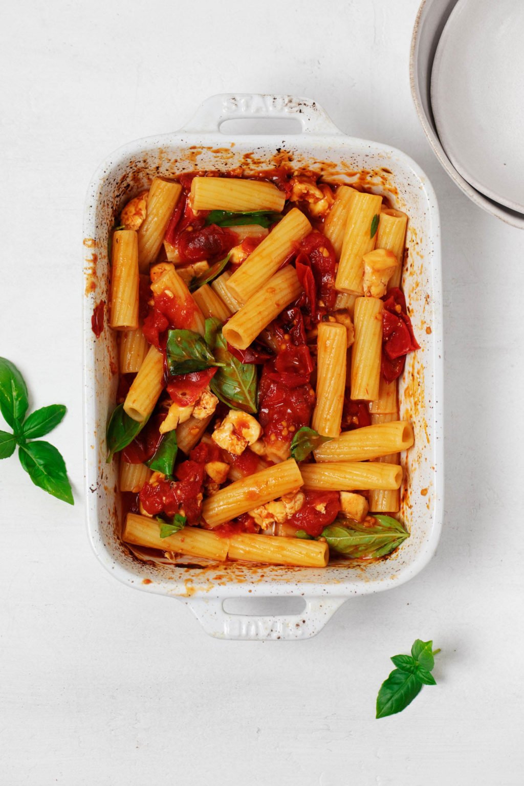 A white, rectangular baking dish has been filled with a vegan feta pasta, topped with fresh herbs.