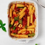 A white, rectangular baking dish has been filled with a vegan feta pasta, topped with fresh herbs.