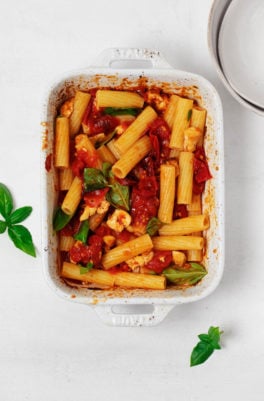 A white, rectangular baking dish has been filled with a vegan feta pasta, topped with fresh herbs.