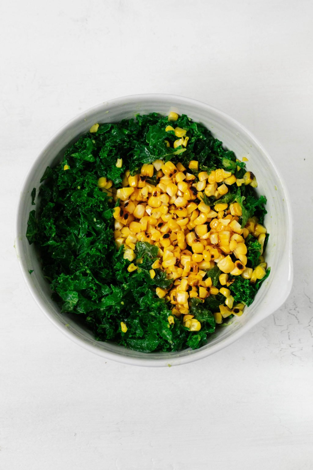 A white mixing bowl has been filled with corn kernels and bright green kale.