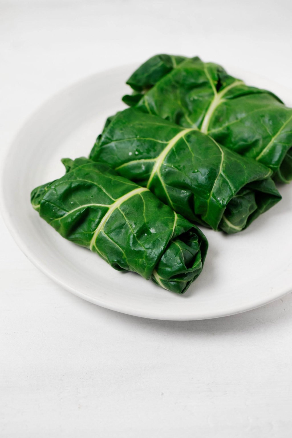 Three large, leafy greens have been steamed, stuffed, and turned into wraps. They rest on a white serving platter.