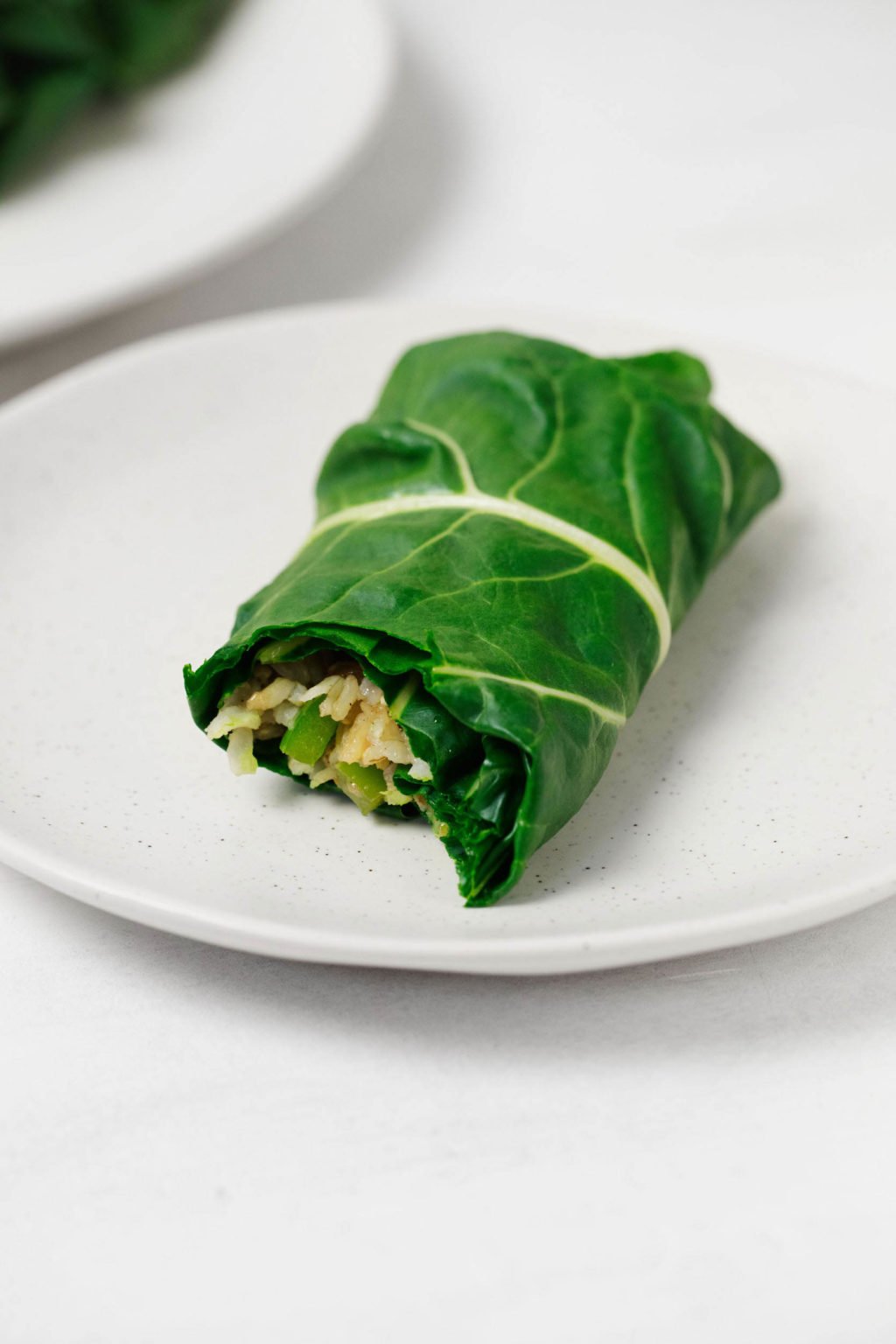 A collard green wrap, stuffed with rice and beans, is resting on a small white plate.