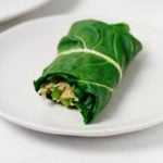 A collard green wrap, stuffed with rice and beans, is resting on a small white plate.