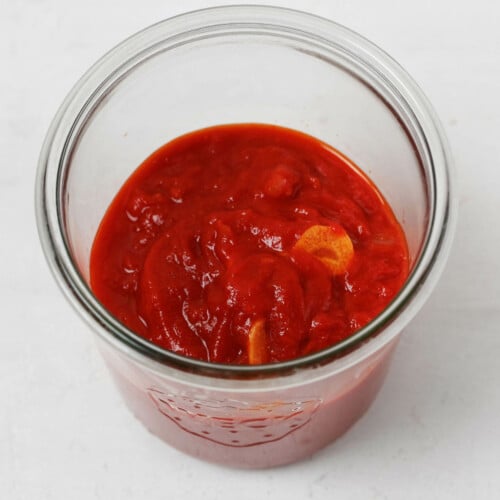A Weck mason jar holds a red pasta sauce, which is studded with garlic.