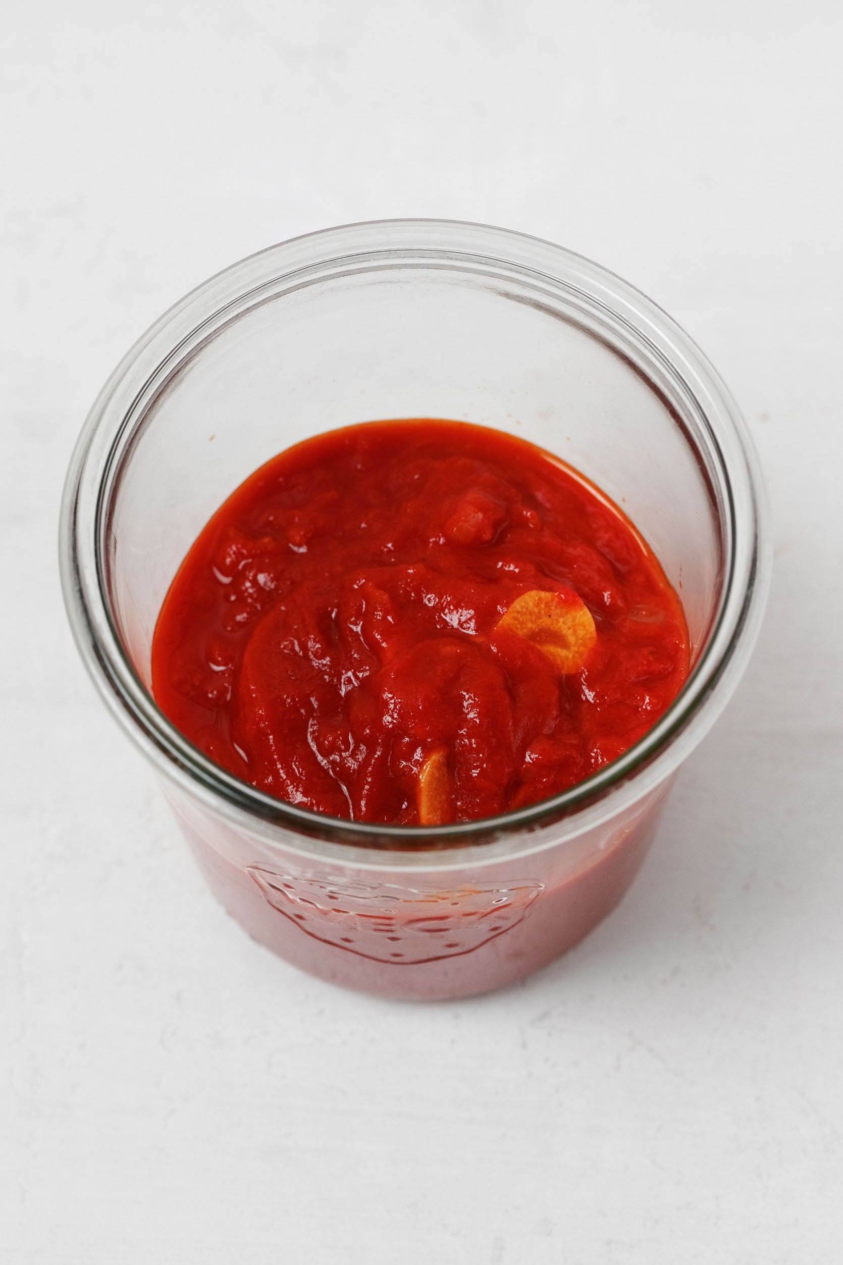 A Weck mason jar holds a red pasta sauce, which is studded with garlic.