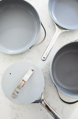 All items in the Caraway Cookware set are resting on a white, marbled surface.