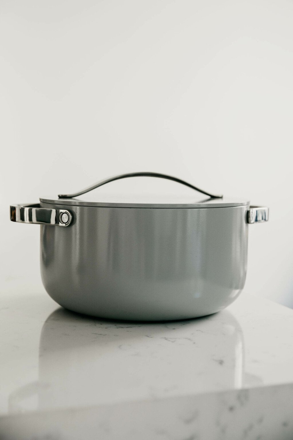 A gray, ceramic pot with stainless steel handles rests on a marble countertop.